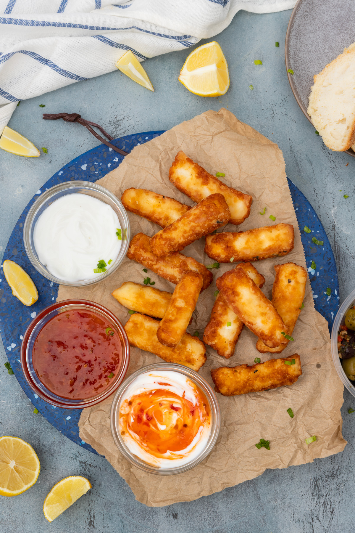 A blue marble platter of halloumi fries with 3 small bowls of dips from above on a blue background 