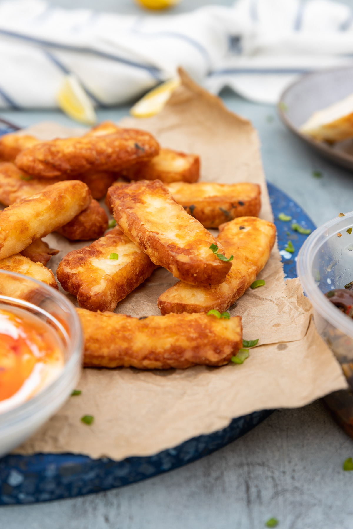 A stack of halloumi fries on brown paper and a blue marble platter with dips to the side