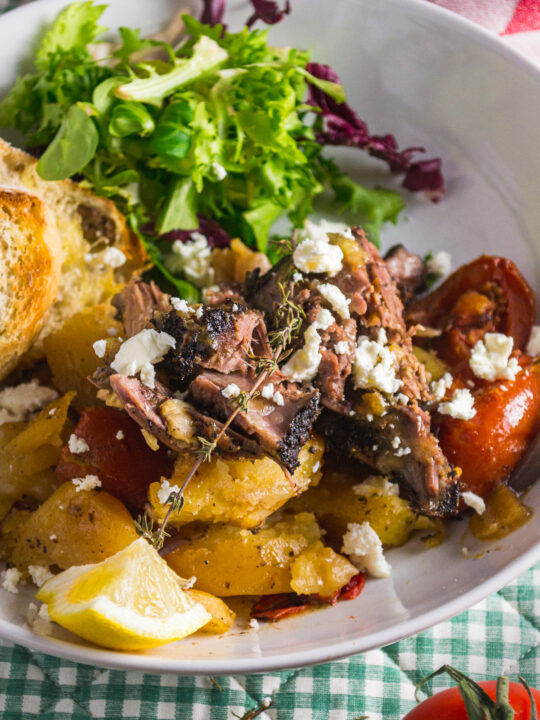 Closeup of a dish of slow roasted Greek lamb in a white dish with colourful garnishes such as feta and lettuce