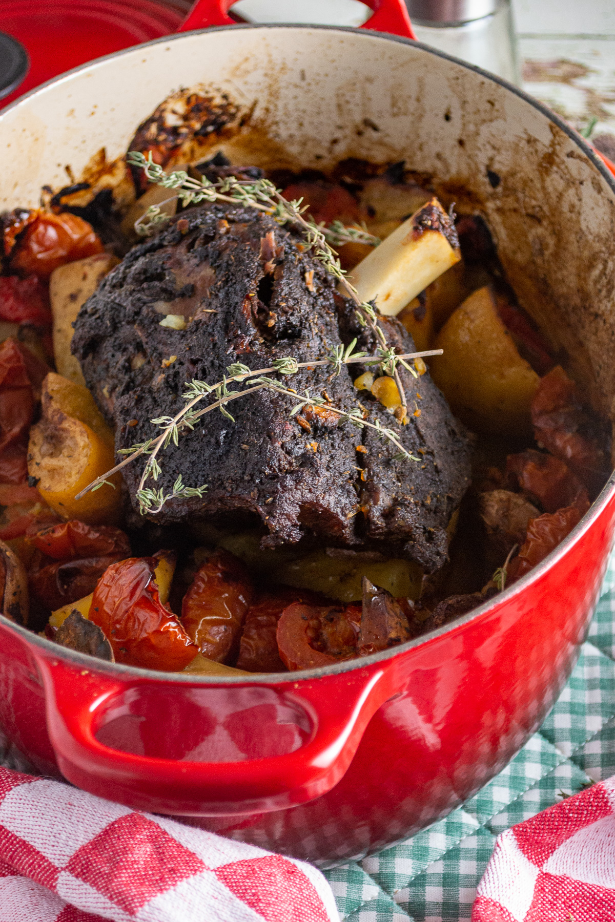 Just cooked Greek lamb leg on a bed of potatoes and vegetables in a red cast iron pot