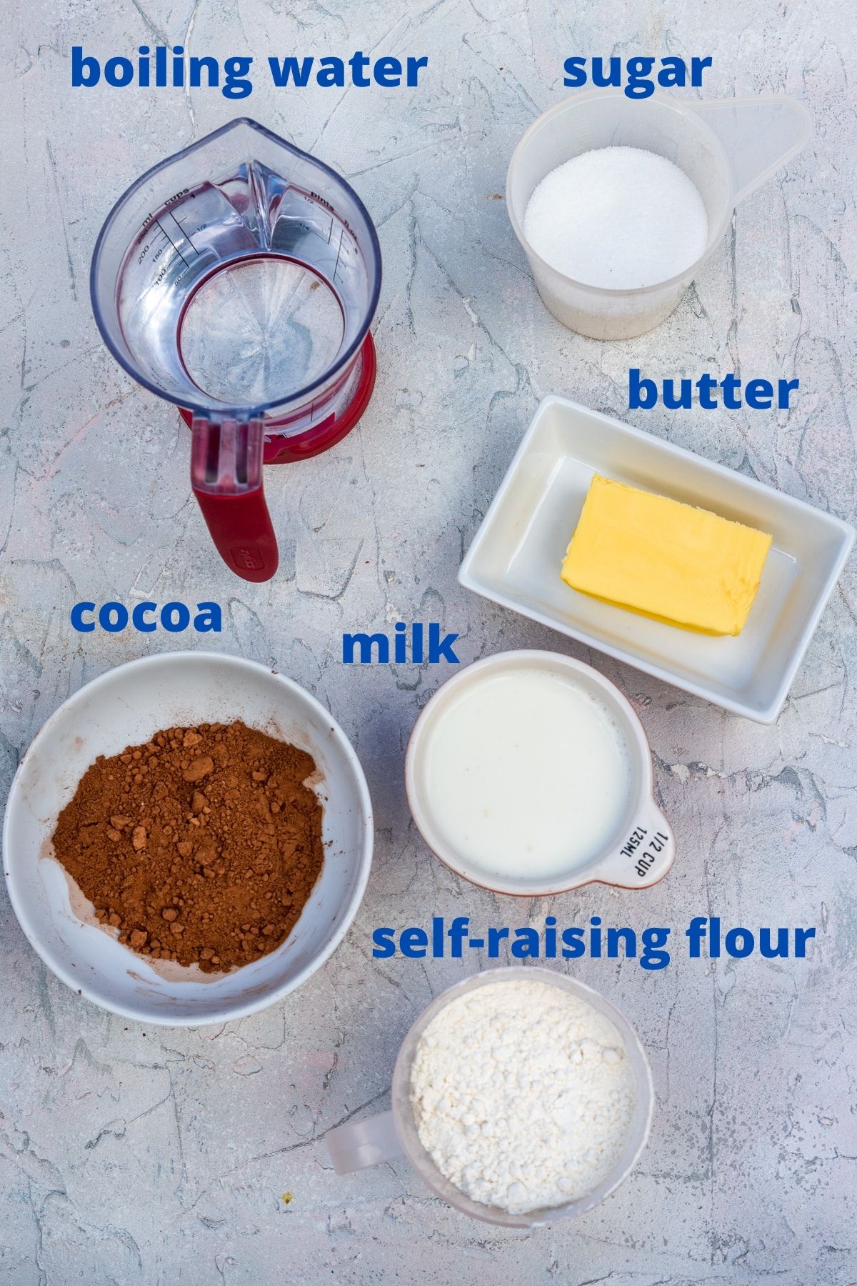 Ingredients for self-saucing chocolate pudding from above including jug of boiling water, sugar, butter, cocoa, milk and self-raising flour