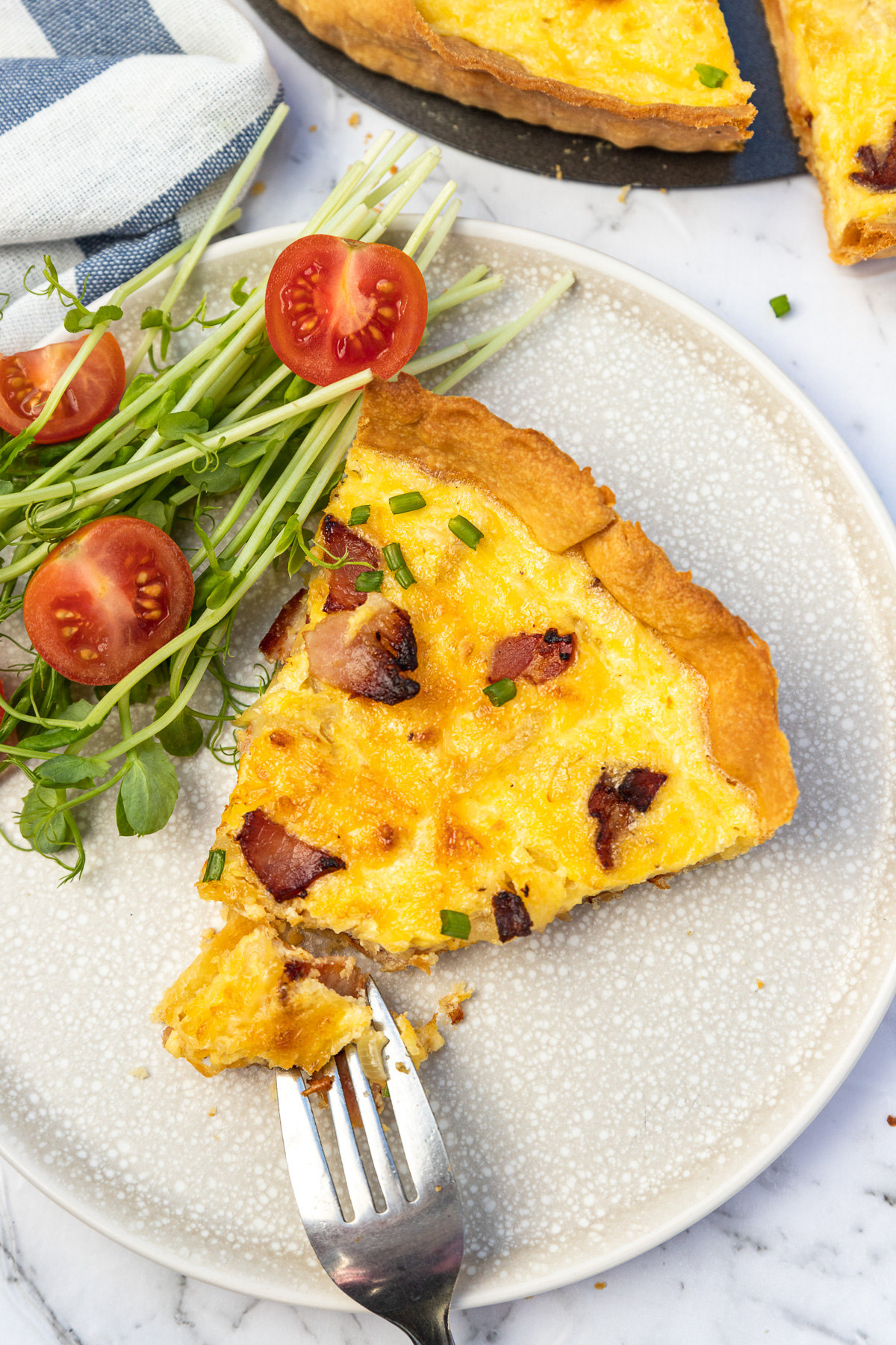 Slice of quiche and fork on a light beige plate with side salad photographed from above.