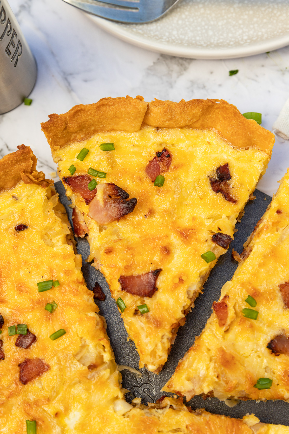 Closeup of a slice of quiche cut from a whole quiche lorraine photographed from above.