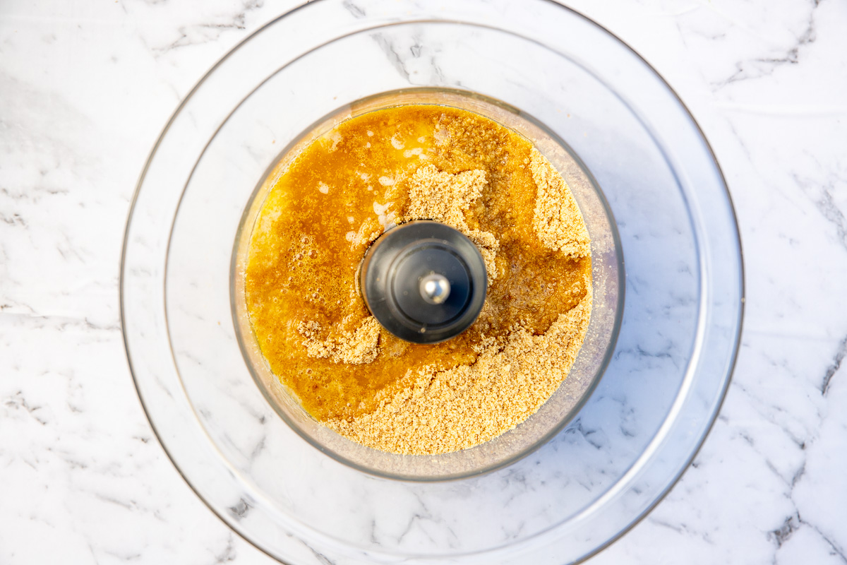 biscuit crumbs and butter in a food processor from above on a marble background