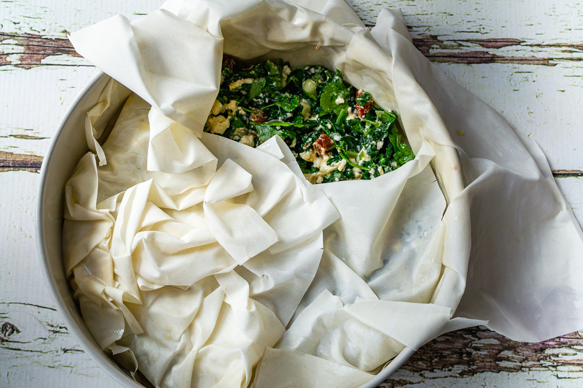 Overhead view of a spinach and feta filo pie with a bit of the filling exposed and in a springform pan.