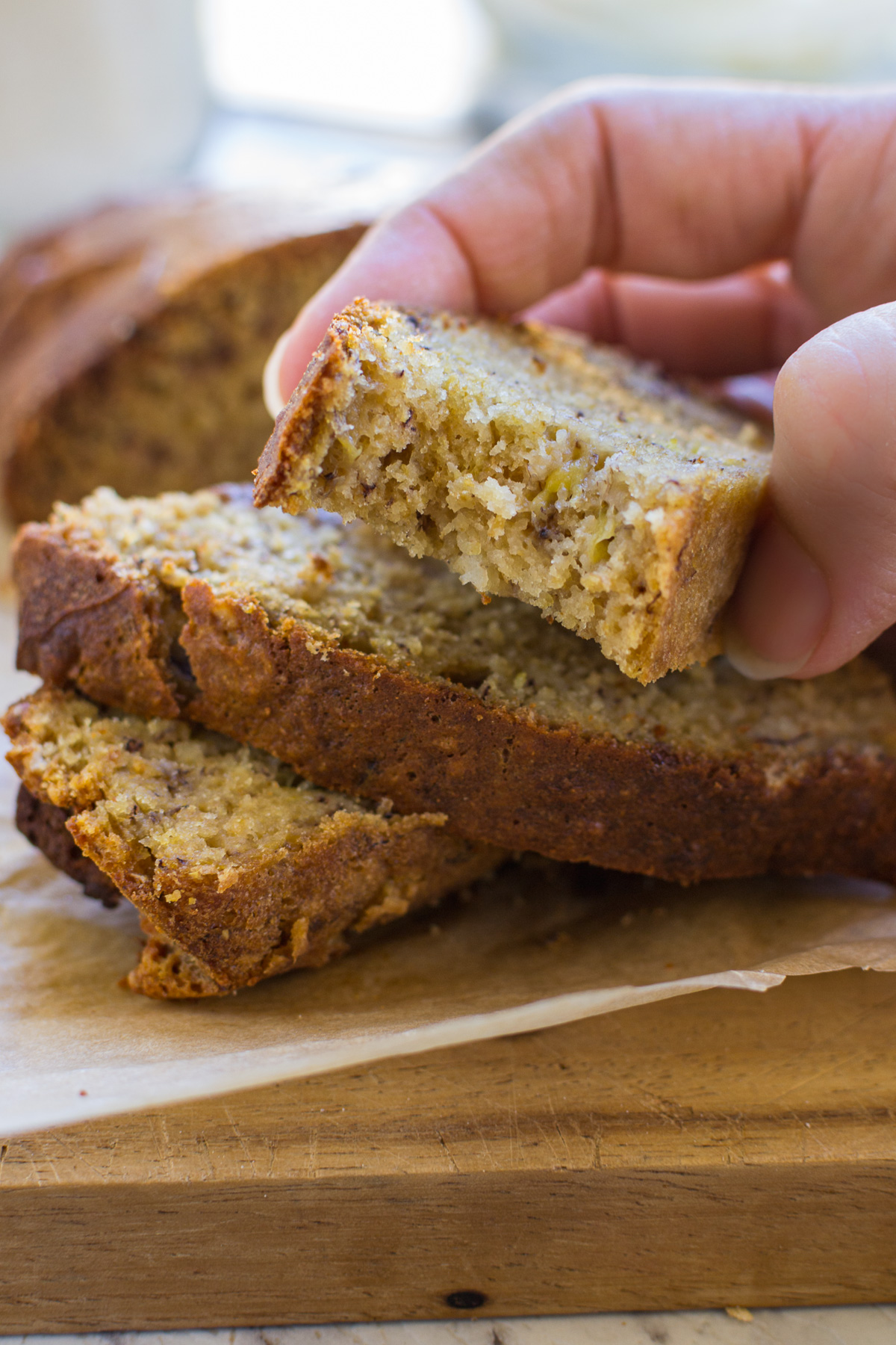 Someone holding up a slice of banana bread with a bite out of it and with more in a pile underneath.