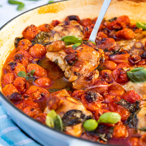 A closeup of someone spooning chicken and chorizo with cherry tomatoes out of a blue cast iron pan.
