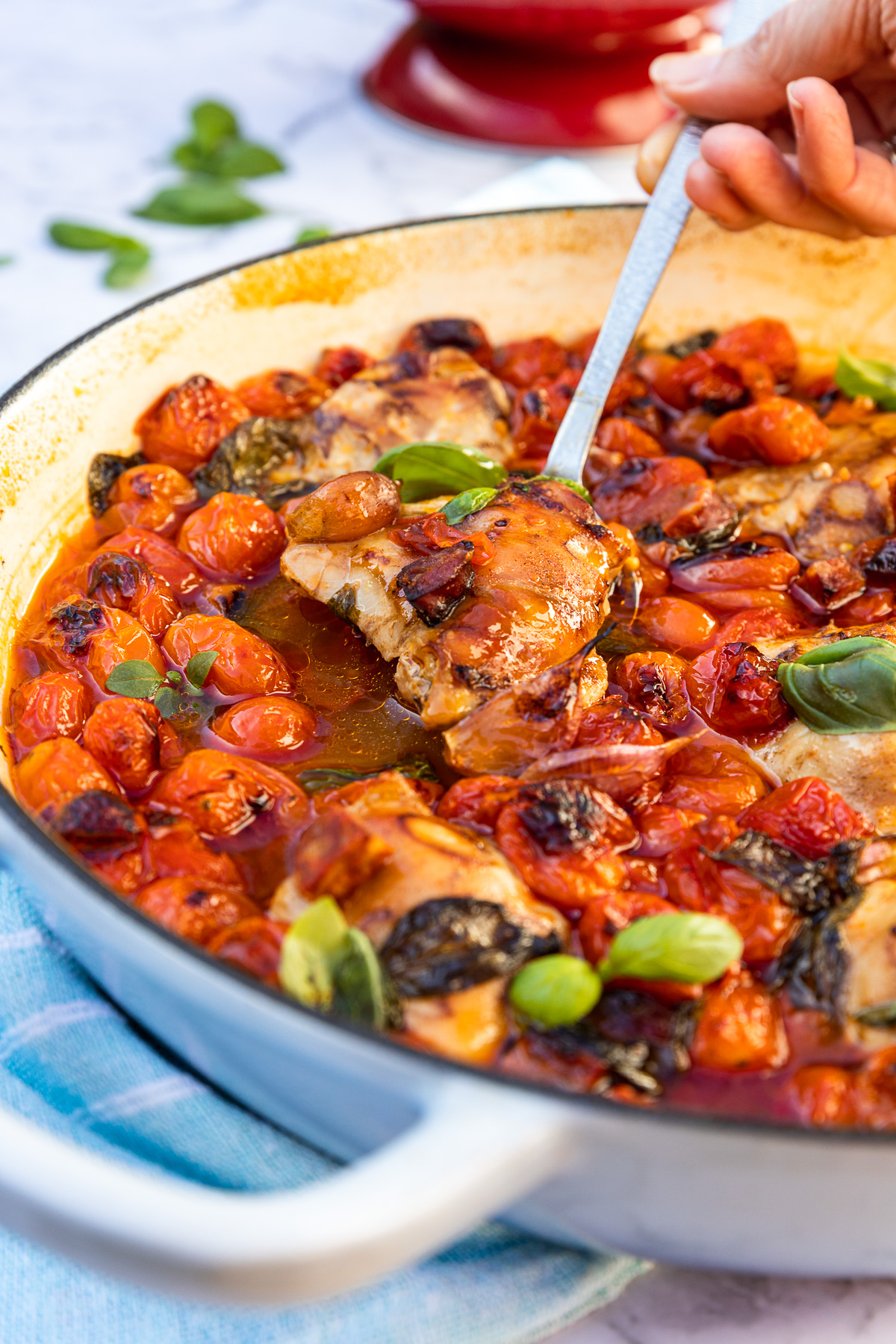 A closeup of someone spooning chicken and chorizo with cherry tomatoes out of a blue cast iron pan.