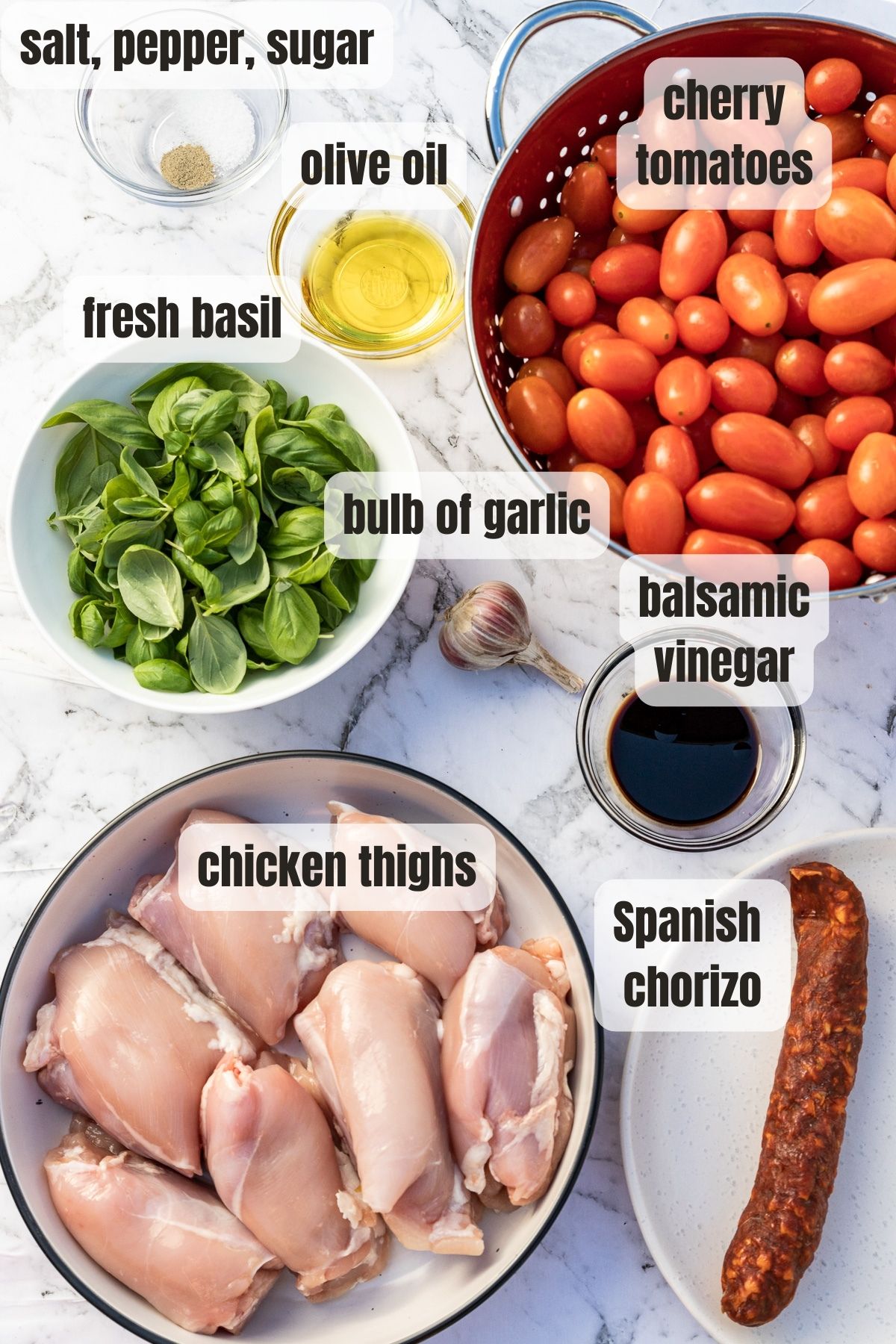 An overhead photo of all the ingredients needed for chicken and chorizo tray bake including chicken thighs, chorizo sausage, garlic, basil and cherry tomatoes.