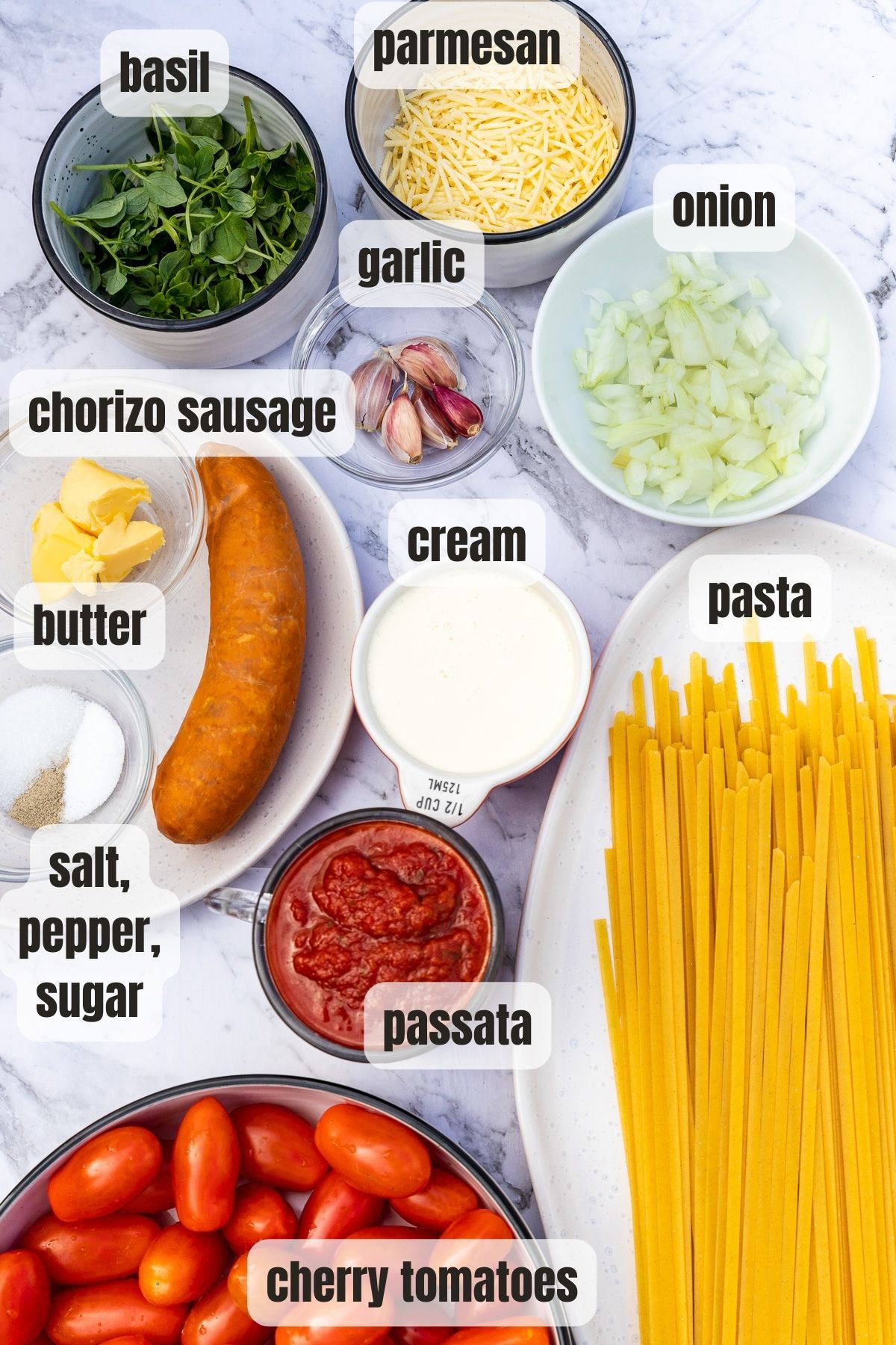 All the ingredients needed to make creamy chorizo pasta on a marble background and labelled.