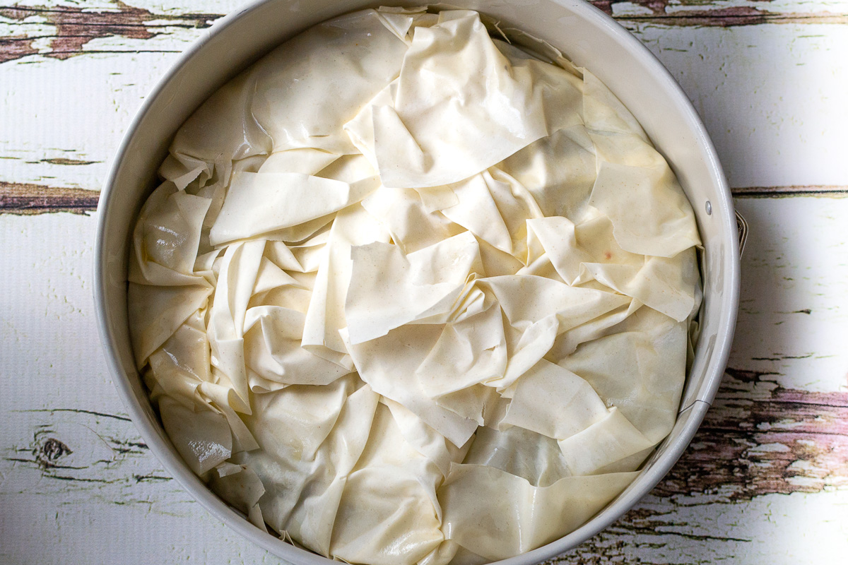 Overhead view of an unbaked spinach and feta filo pie in a springform pan on a white wooden background.