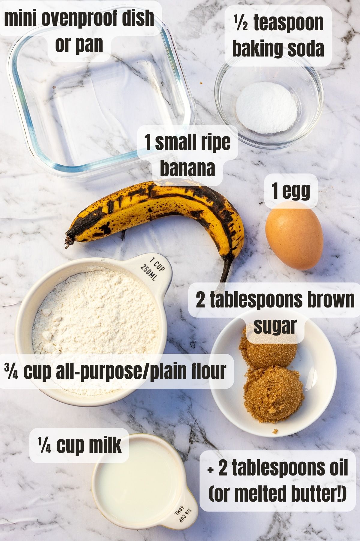 All the ingredients needed to make mini air fryer banana bread including flour, an egg, milk, a ripe banana and oil, on a marble background.