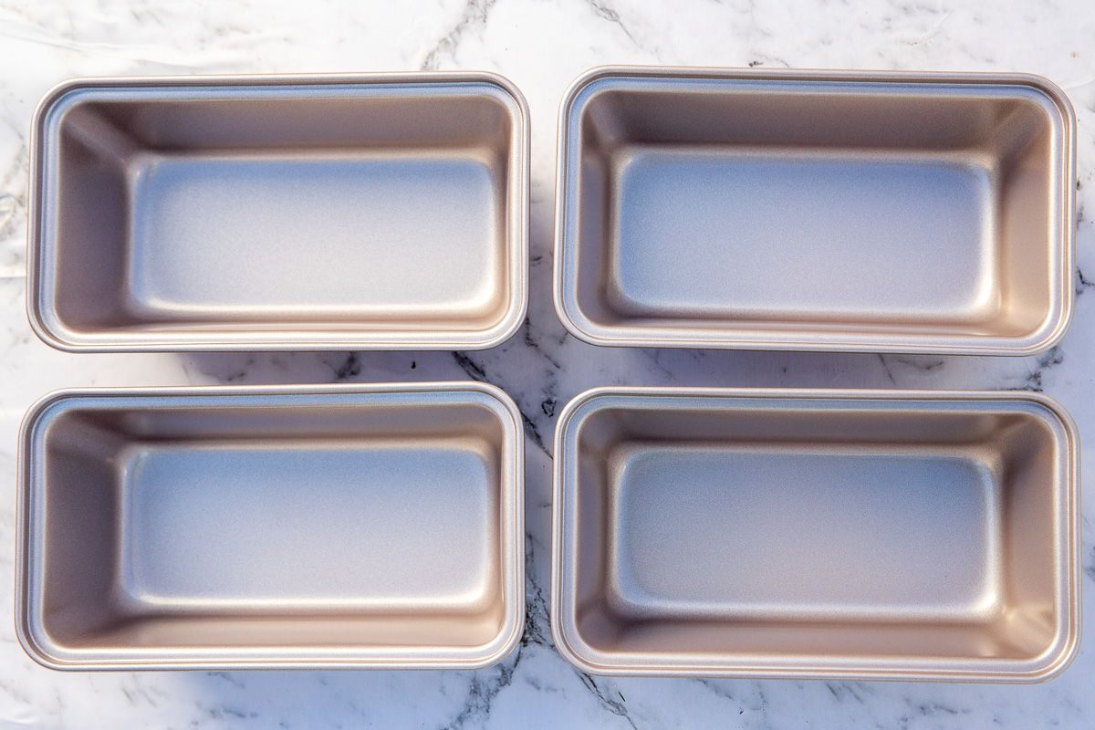 Set of 4 mini loaf pans in a rose gold color on a marble background.
