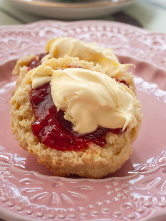 Closeup of a 3 ingredient lemonade scone topped with strawberry jam and cream on a decorative pink plate.