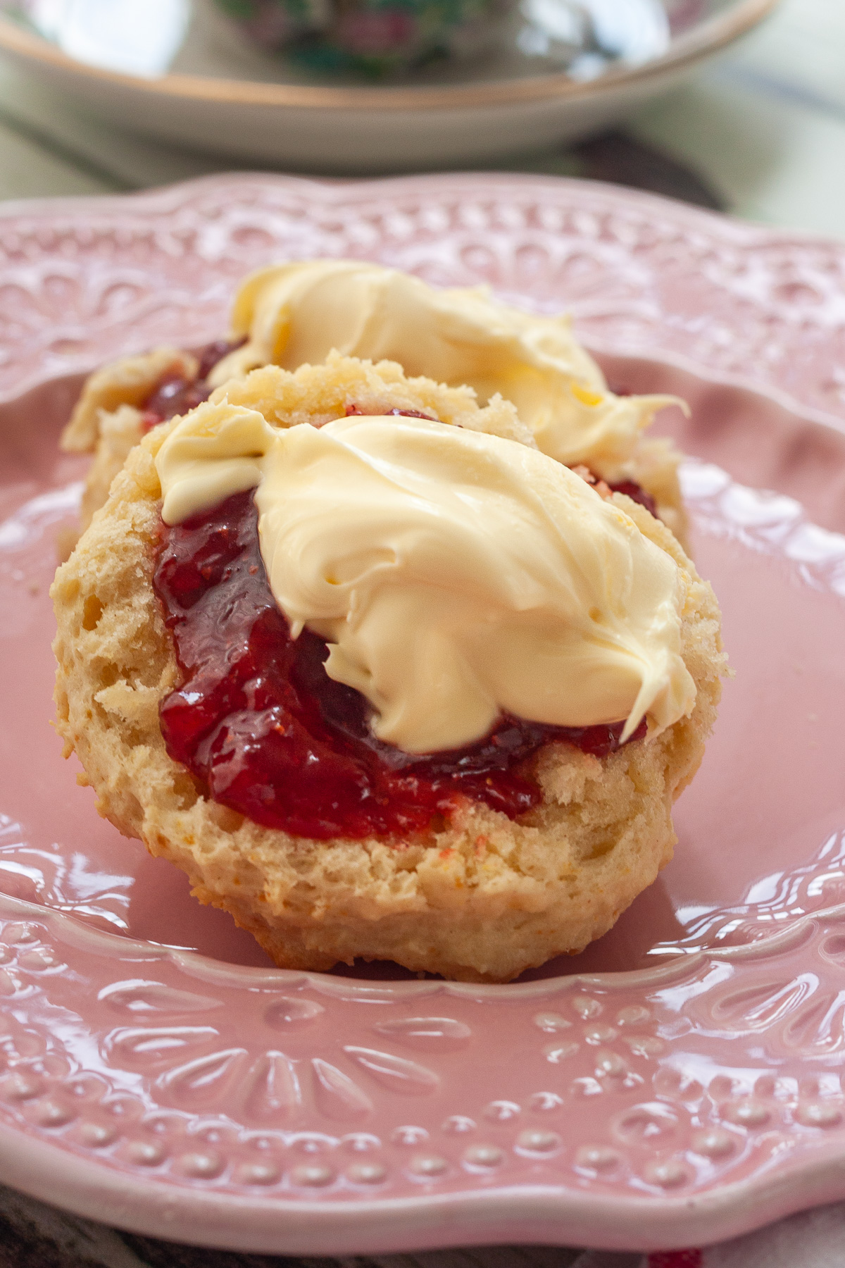 Closeup of a 3 ingredient lemonade scone topped with strawberry jam and cream on a decorative pink plate.