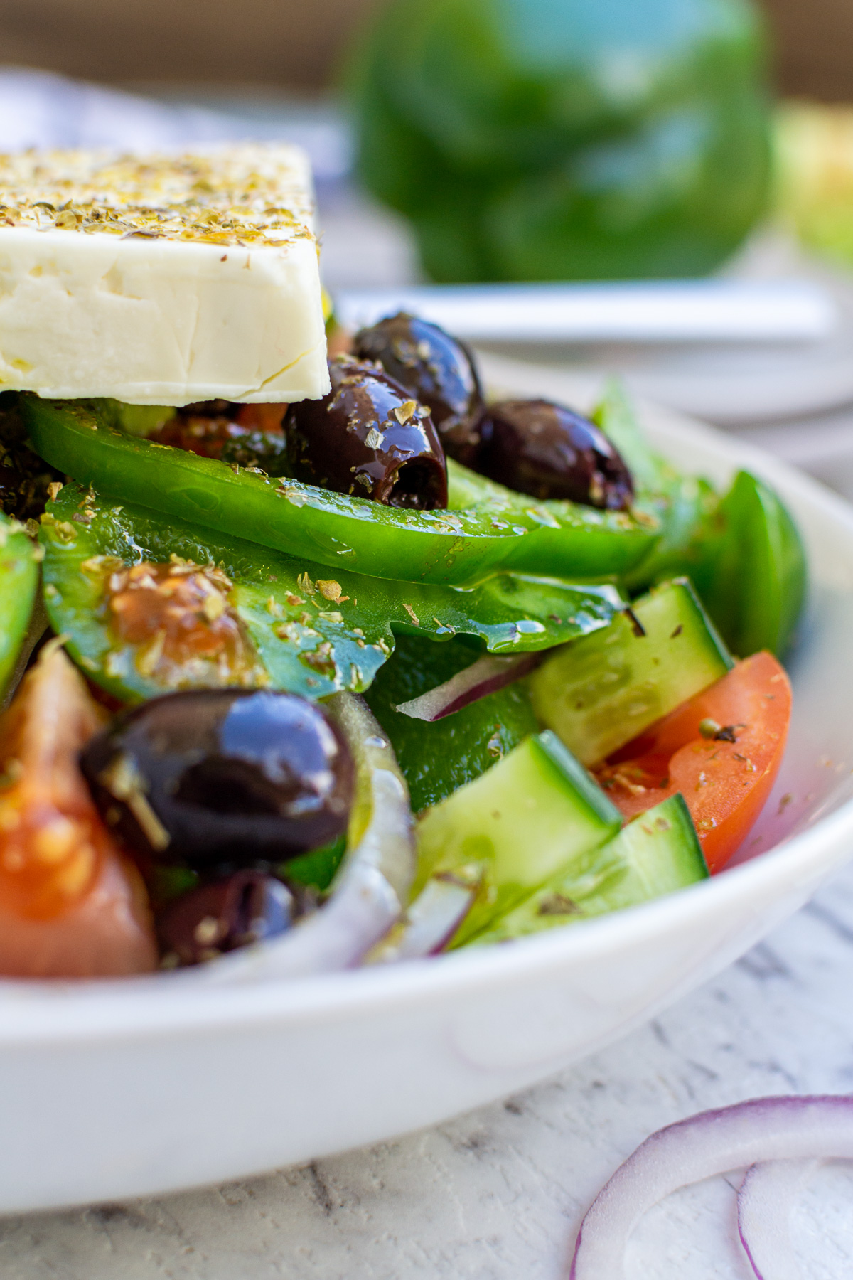 Closeup of part of a dish of traditional Greek salad in a white bowl on a marble background.