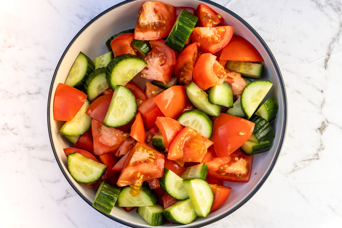 Chopped tomatoes and cucumber in a big bowl from above for making a Greek salad.