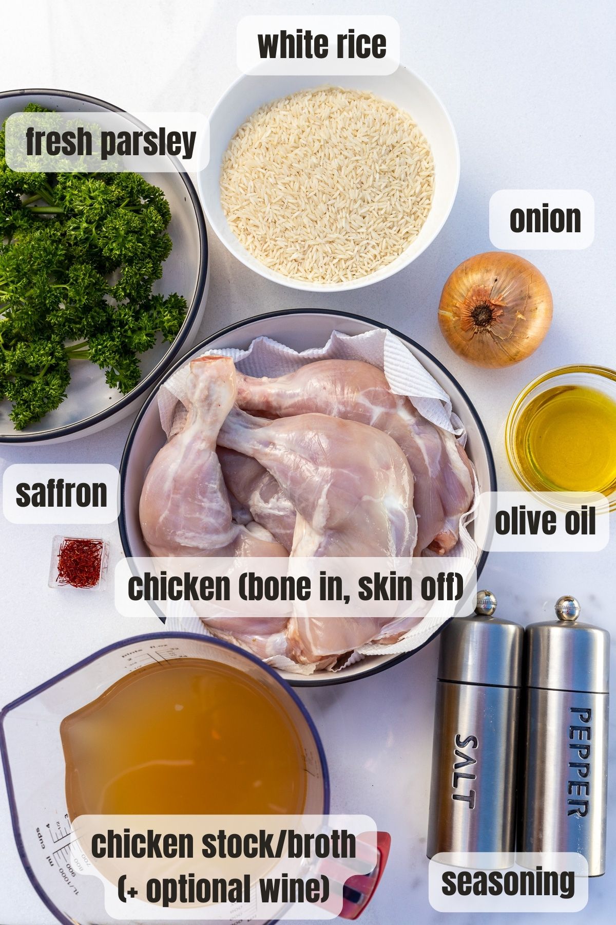 Overhead of all the ingredients to make stovetop chicken and rice including chicken with the bone in and skin off, olive oil, onion, rice, fresh parsley, saffron and seasoning..