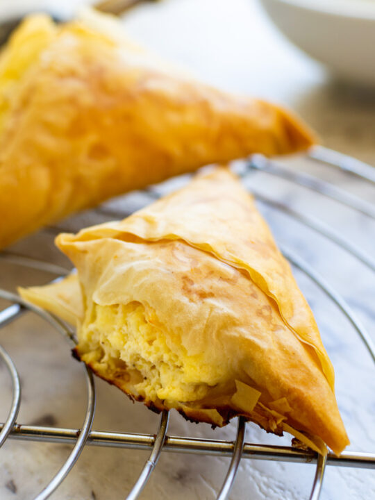 A mini Greek cheese pie just baked on a cooling rack and marble background with another pie in the background.