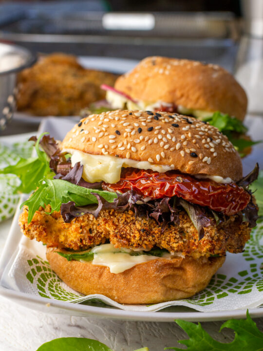 A closeup of an air fryer crispy chicken burger on a green and white patterned napkin and rectangular white plate with another burger in the background.