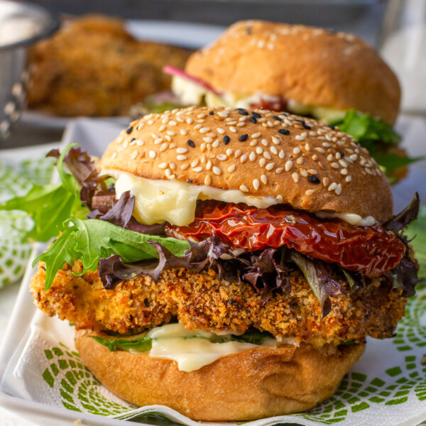 A closeup of an air fryer crispy chicken burger on a green and white patterned napkin and rectangular white plate with another burger in the background.