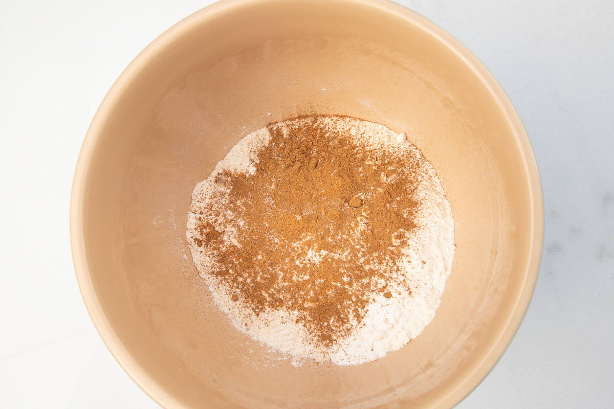 Overhead image of flour, baking soda and baking powder and cinnamon and nutmeg in a baking bowl.