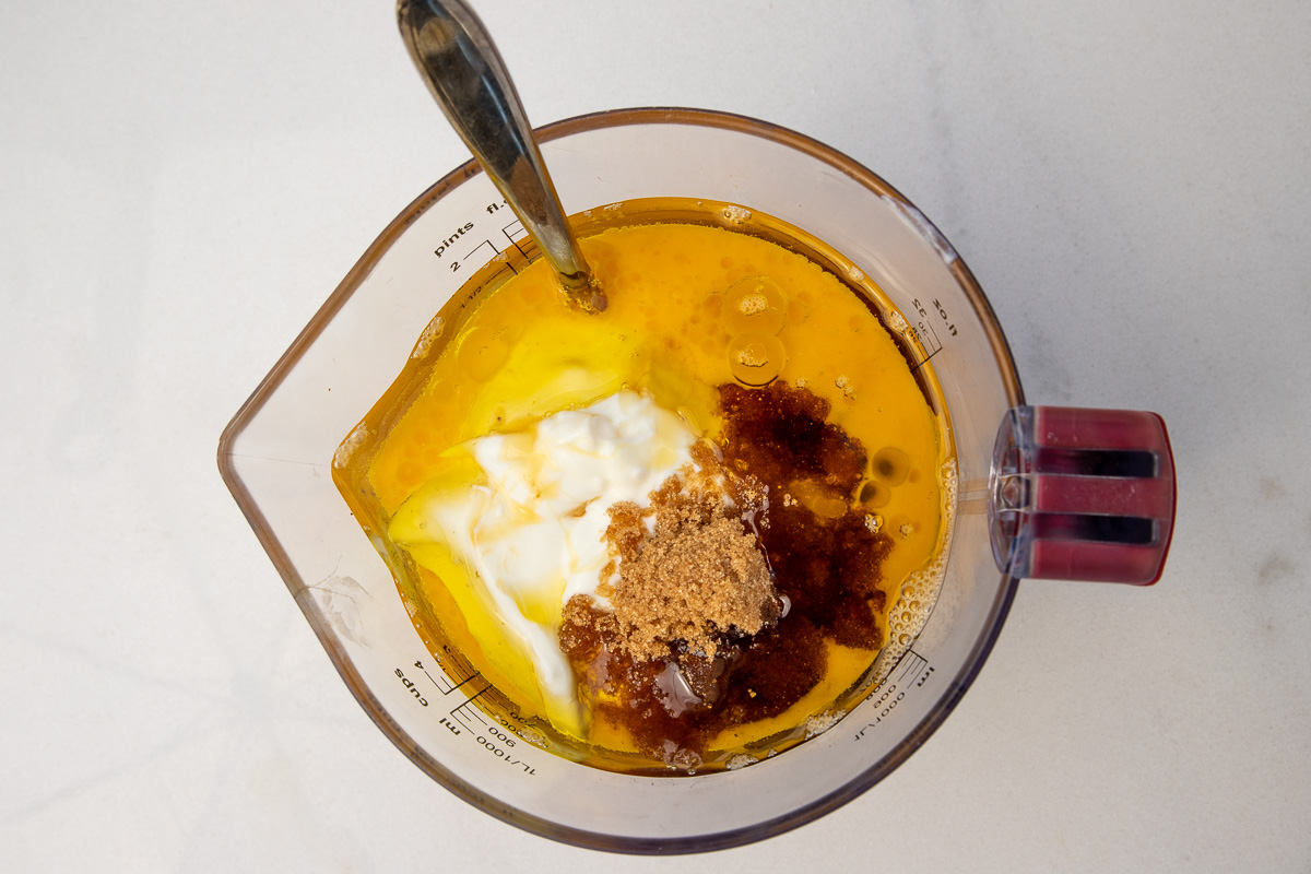 Overhead view of all the wet ingredients for Greek yogurt banana muffins in a jug including yogurt, brown sugar, honey, eggs and oil.