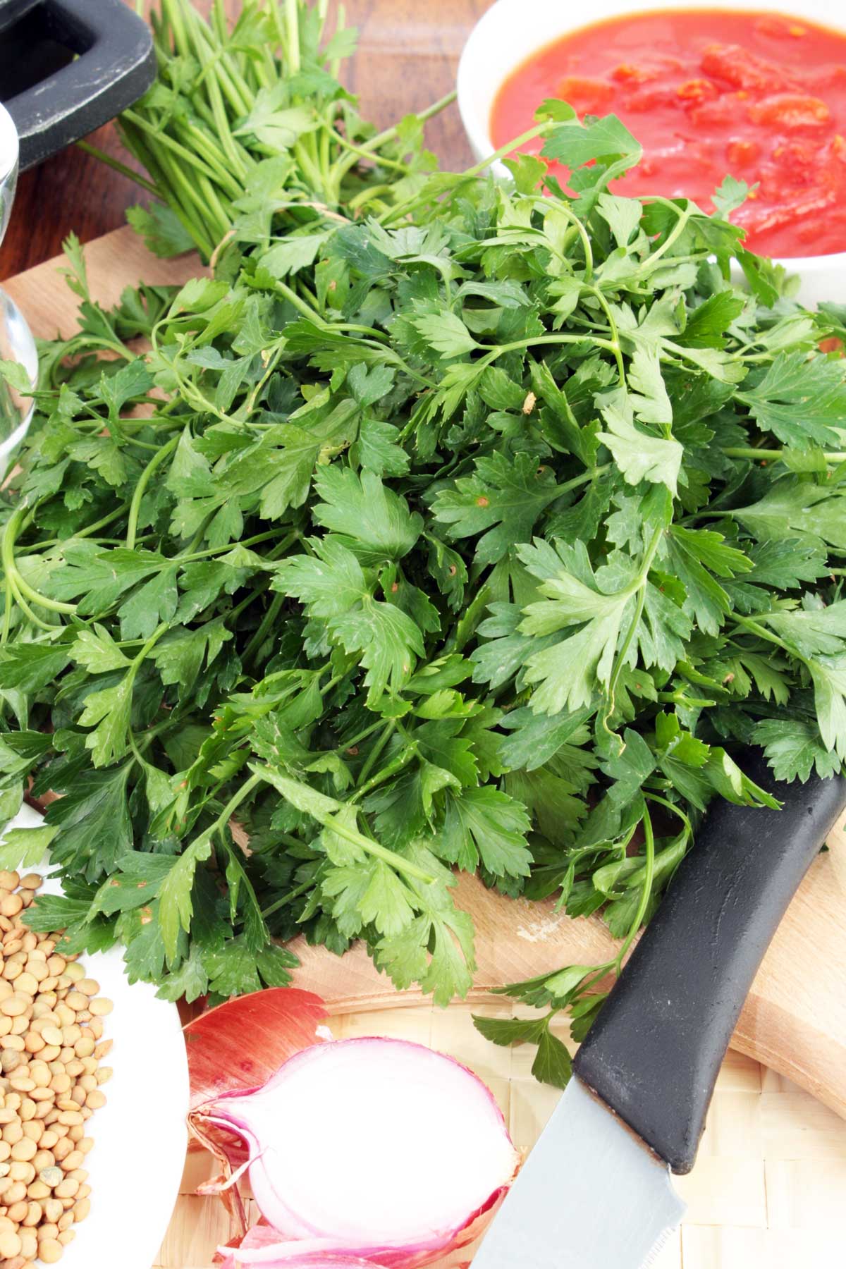 A bunch of fresh parsley on a chopping board with a knife and other ingredients for a soup.