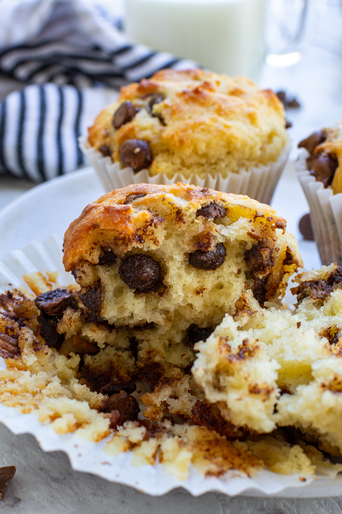 A Greek yogurt chocolate chip muffin ripped open to expose the inside on a paper liner and with another muffin in the background.