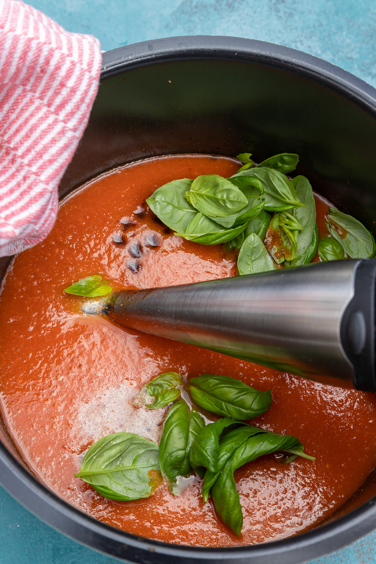 Closeup of an immersion blender in an instant pot of tomato soup with fresh basil and balsamic vinegar on top.