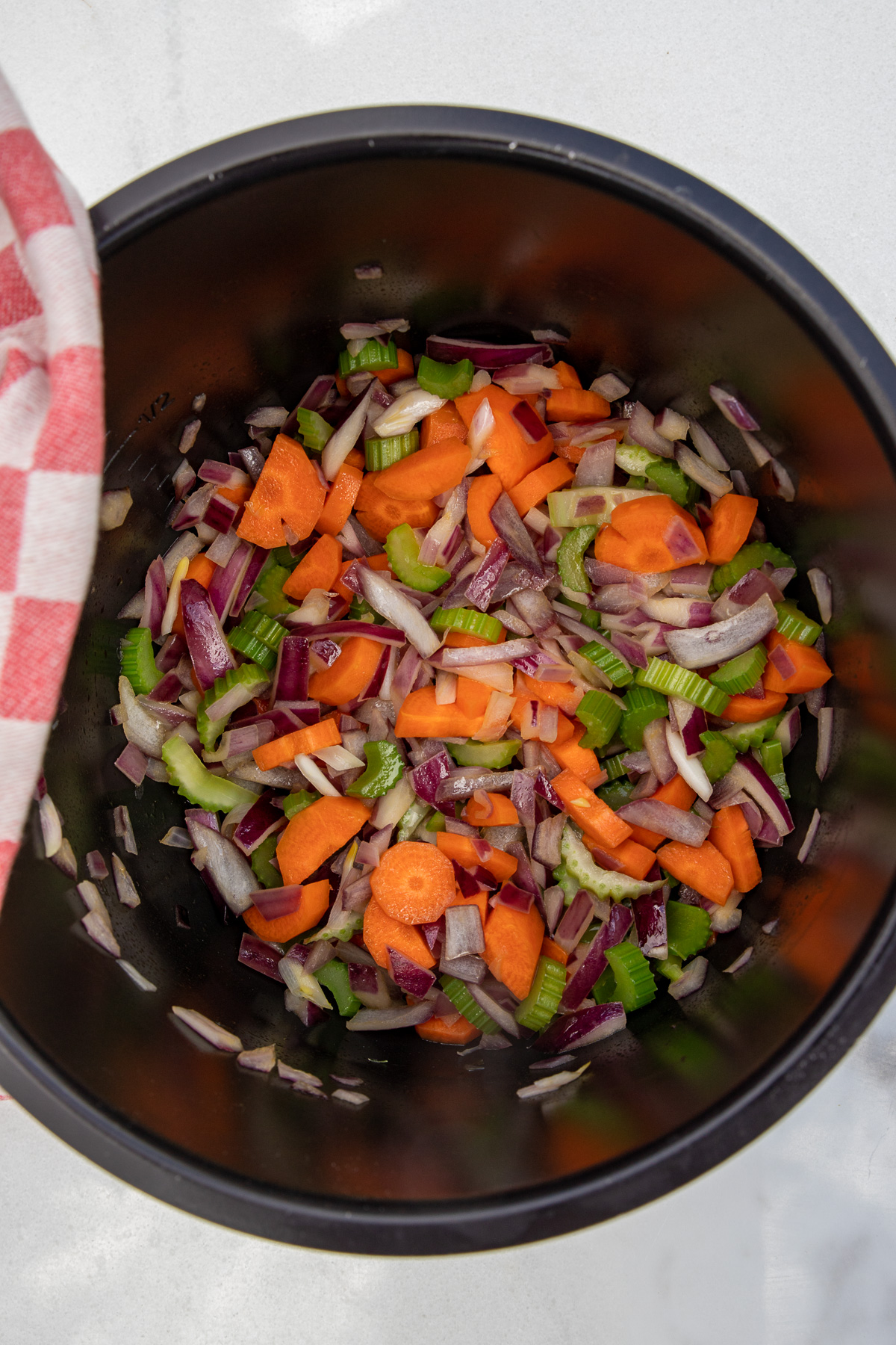 Closeup overhead shot of chopped carrots, celery and onion in an instant pot ready to make soup, all on a marble background.