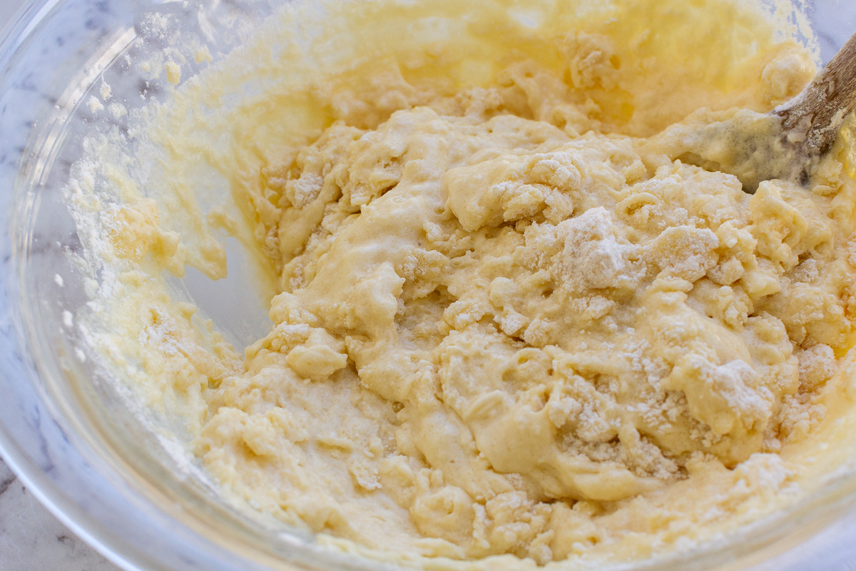 Closeup of Greek yogurt muffin batter in a big glass bowl on a marble background and with a wooden spoon in it.