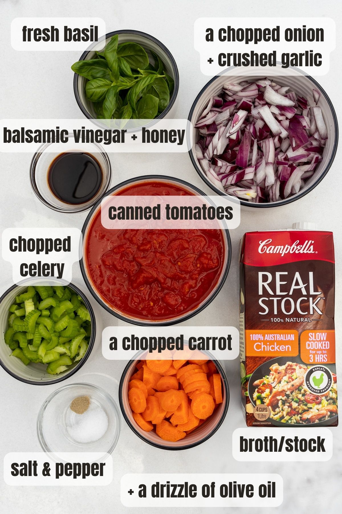 Overhead of all the ingredients needed to make instant pot tomato soup including canned tomatoes, chopped carrots, celery and onion, chicken broth, salt and pepper, balsamic vinegar, honey, and fresh basil.