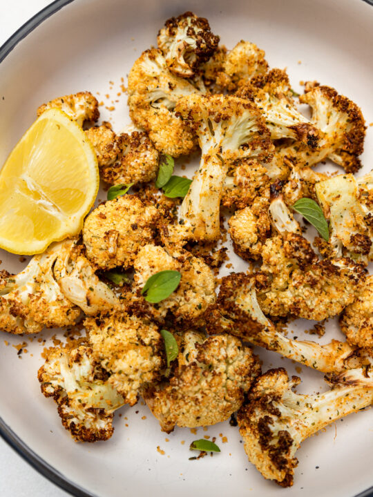 Closeup of an overhead view of a big bowl of air fried cauliflower with lemon and fresh herbs on top.