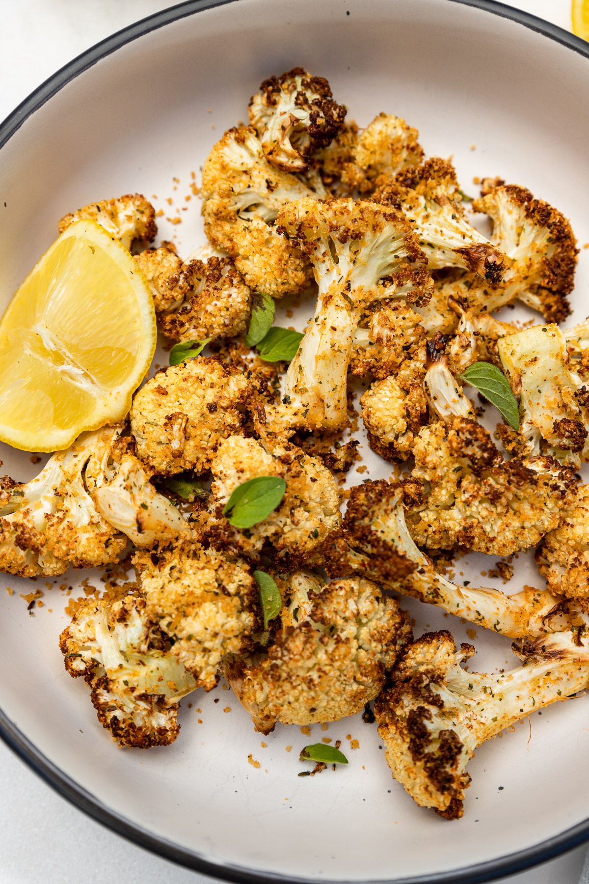 Closeup of an overhead view of a big bowl of air fried cauliflower with lemon and fresh herbs on top.