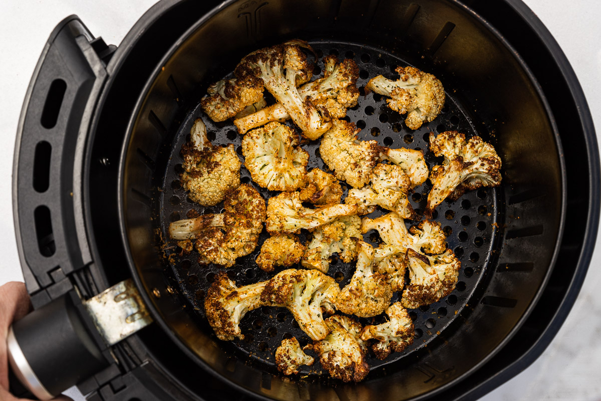 Someone holding an air fryer basket with golden air fried cauliflower in it.