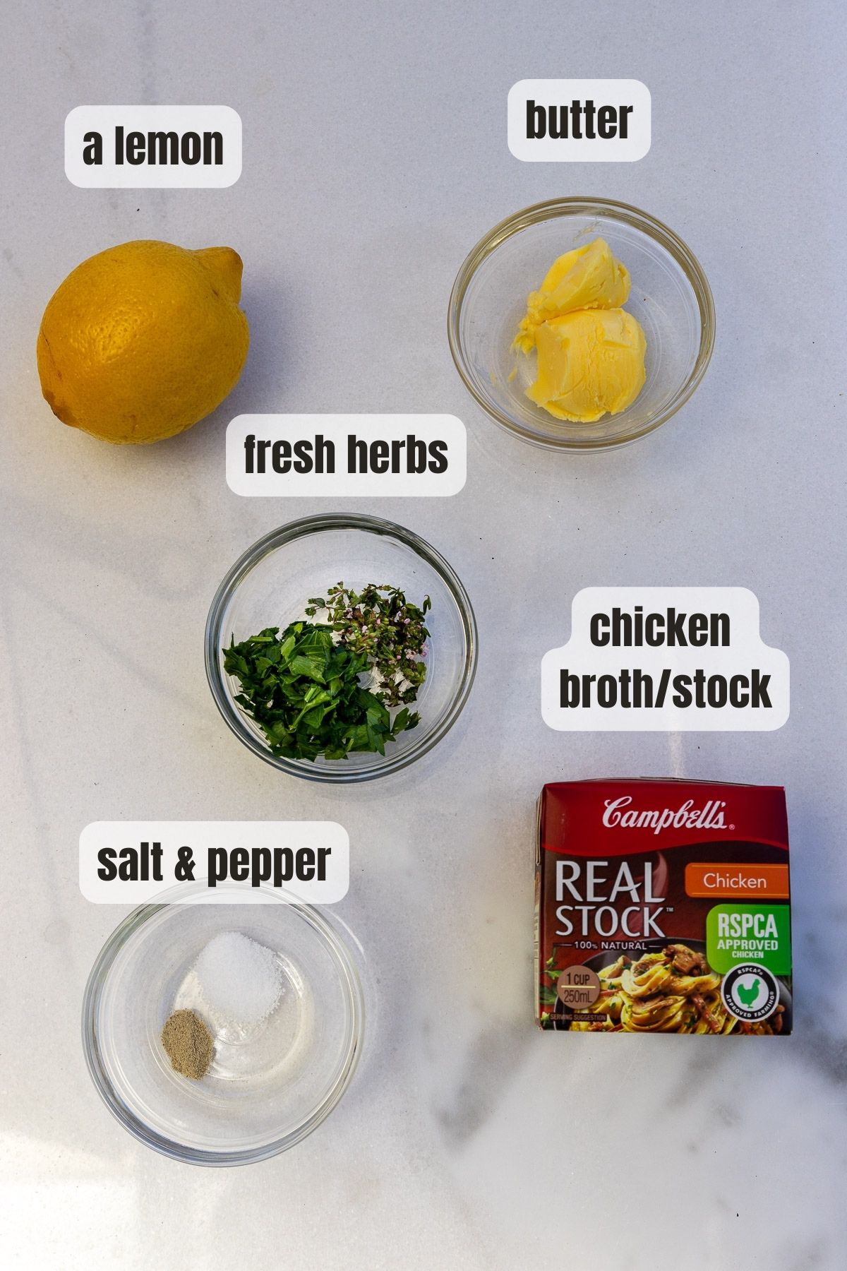 Overhead view of all the ingredients needed to make lemon & butter sauce including a lemon, chicken broth, butter, fresh herbs and salt and pepper.