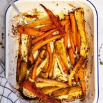 Honey roasted carrots and parsnips with thyme photographed overhead with a black and white checked tea towel in front and fresh thyme at the top, all on a textured white backgrounde.