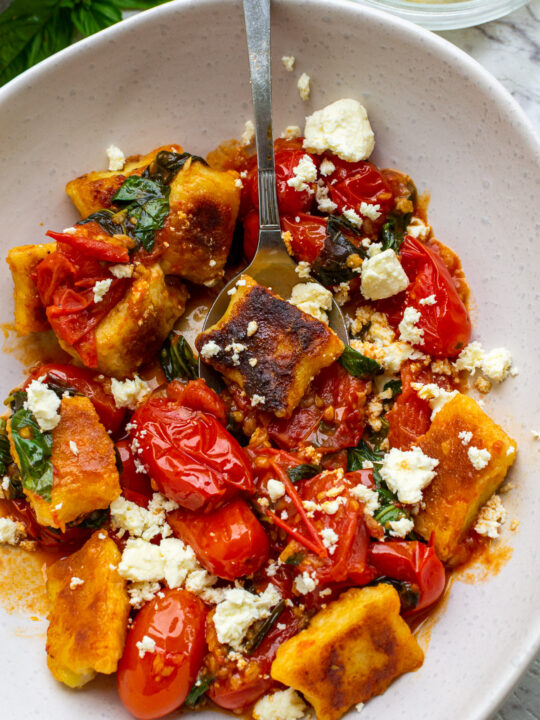 A closeup of an overhead view of a dish of pan-fried gnocchi in cherry tomato basil sauce with feta cheese sprinkled on top.