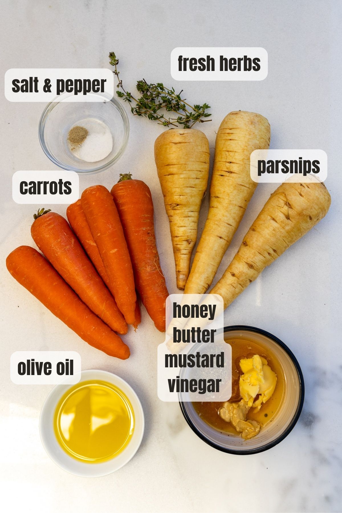 An overhead photo of all the ingredients needed to make honey roast carrots and parsnips including carrots, parsnips, salt and pepper, fresh thyme, olive oil, honey, butter, mustard and vinegar.