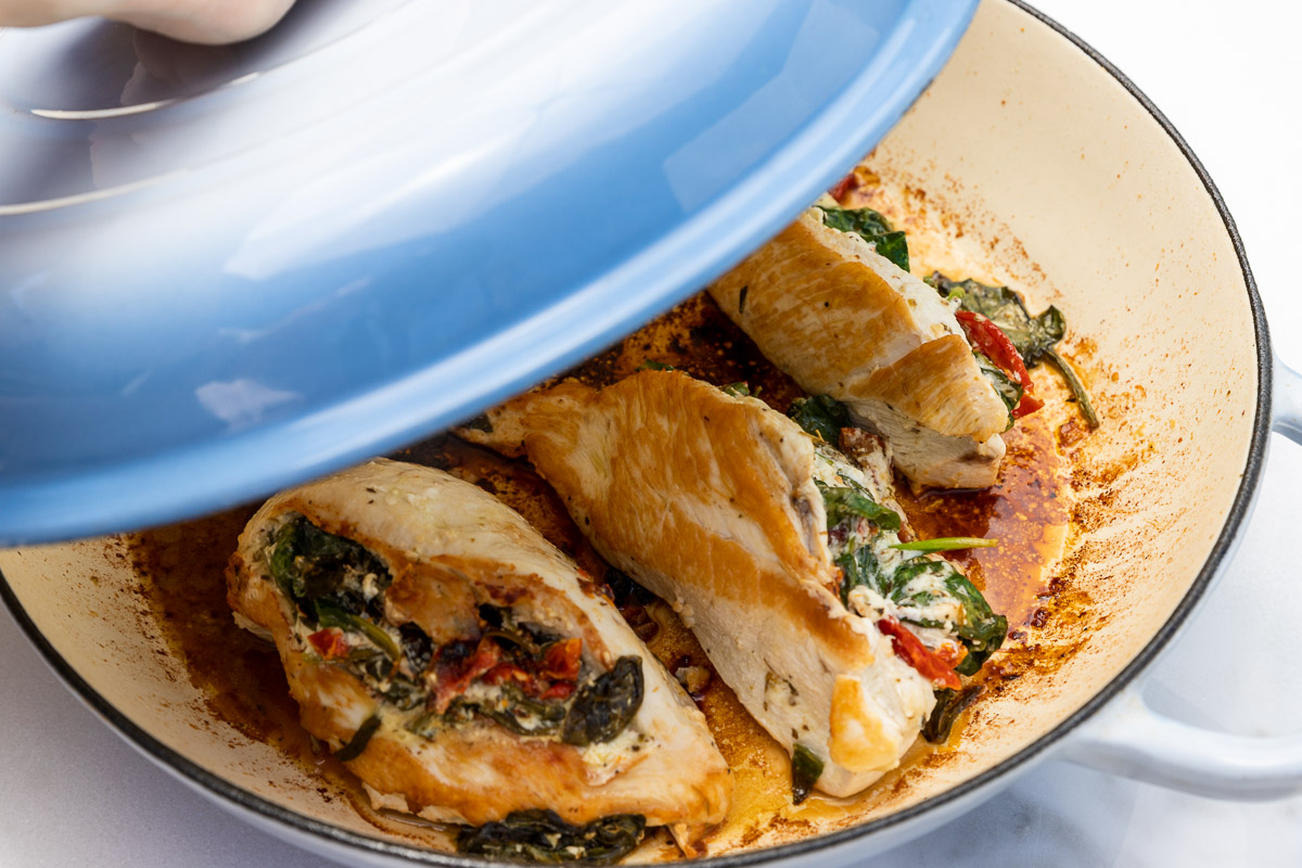 Closeup of spinach feta stuffed chicken in a large blue cast iron pan with the lid half on.