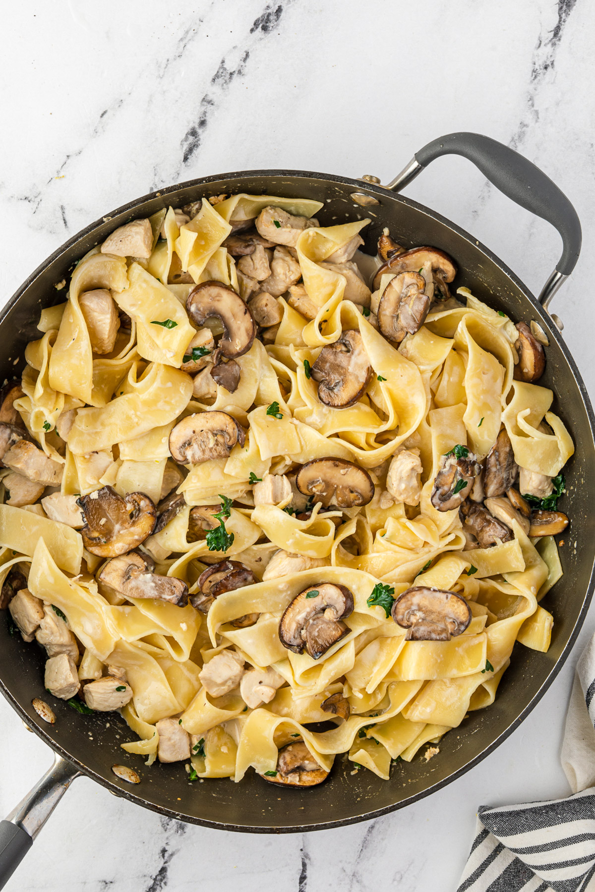 An overhead shot of creamy pappardelle pasta with chicken and mushrooms and fresh parsley in a pan.