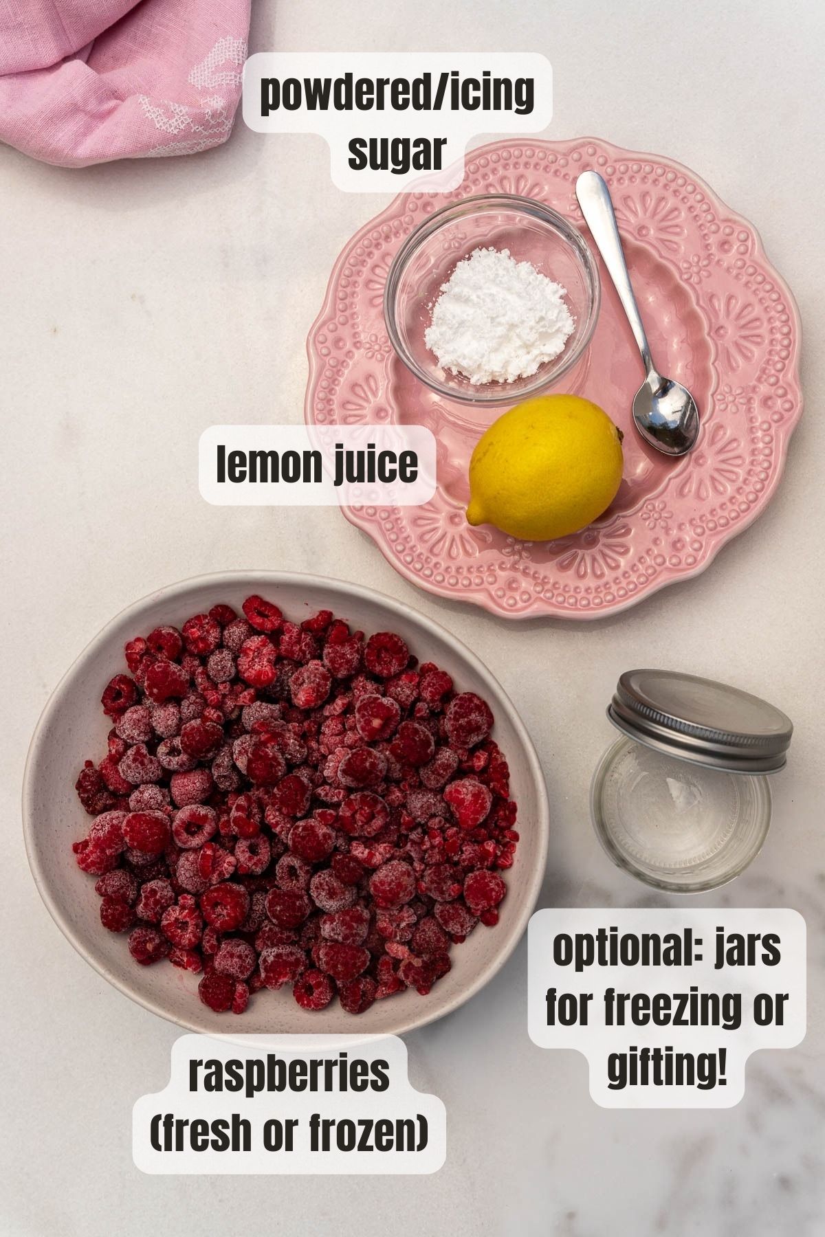 Overhead view of the 3 ingredients for homemade raspberry puree including a bowl of frozen raspberries, a lemon, powdered sugar and an empty jar for possible freezing or gifting.