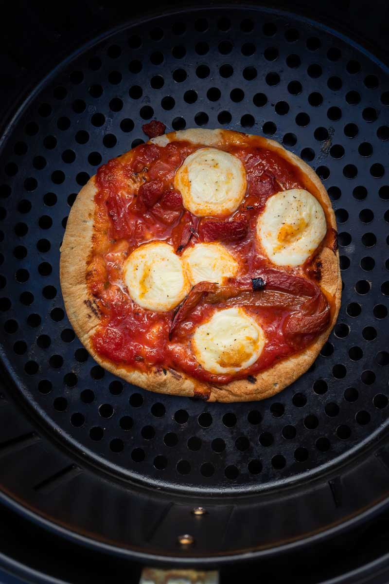 Overhead of a small round pizza cooked in an air fryer with melted mozzarella cheese on top.