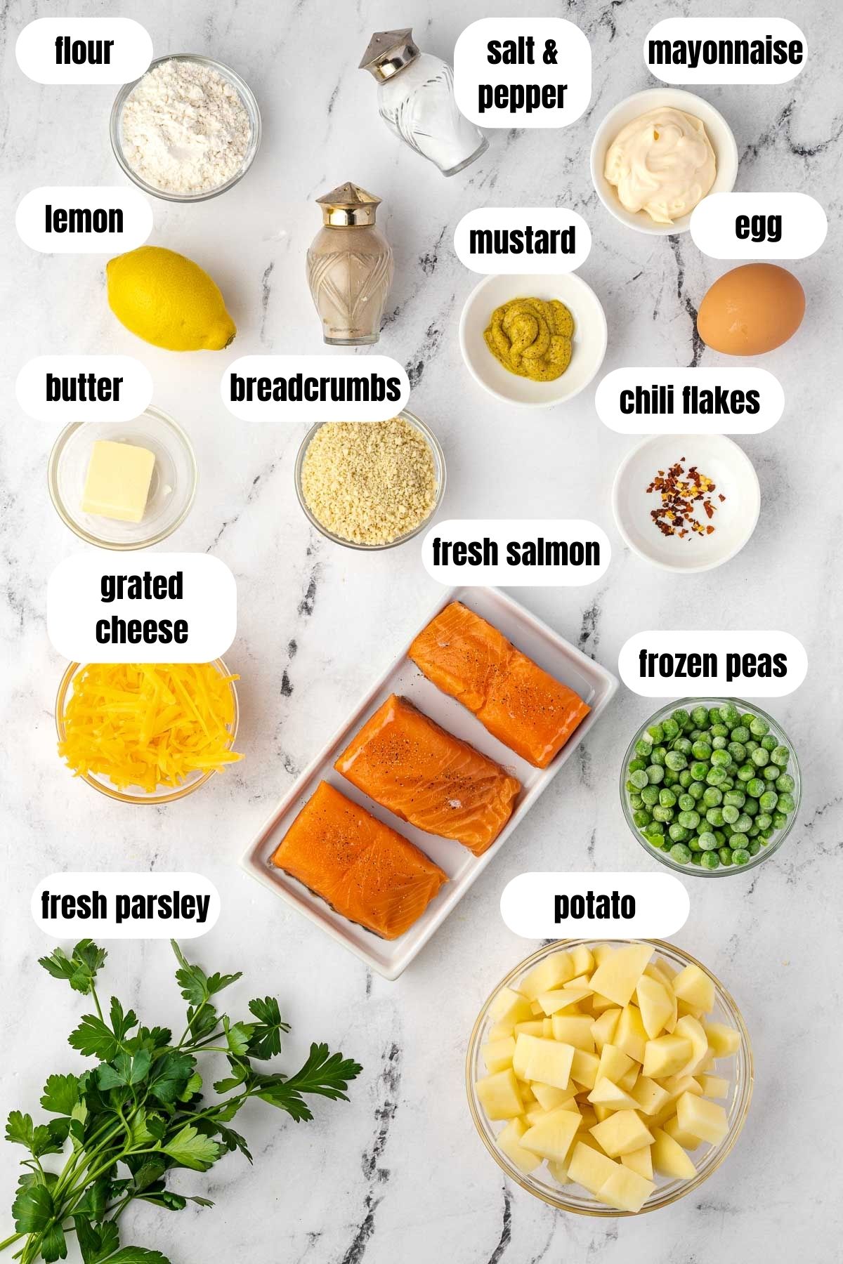 An overhead collage of all the ingredients needed to make crispy salmon fish cakes including fresh salmon, fresh parsley, cubed potato, mustard, flour, grated cheese, a lemon, frozen peas, an egg, chili flakes, breadcrumbs, butter, salt and pepper and mayonnaise.