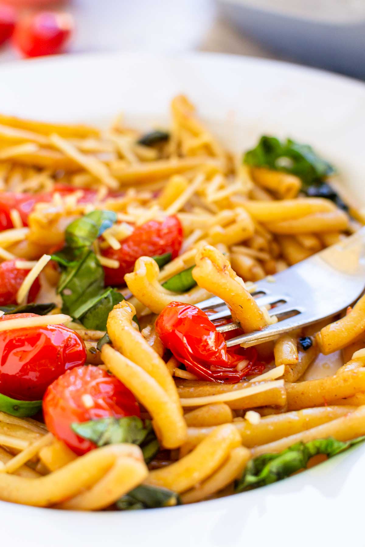 Closeup of someone picking up some casarecce pasta in a simple cherry tomato and basil sauce, with the rim of the white plate in the foreground and background.