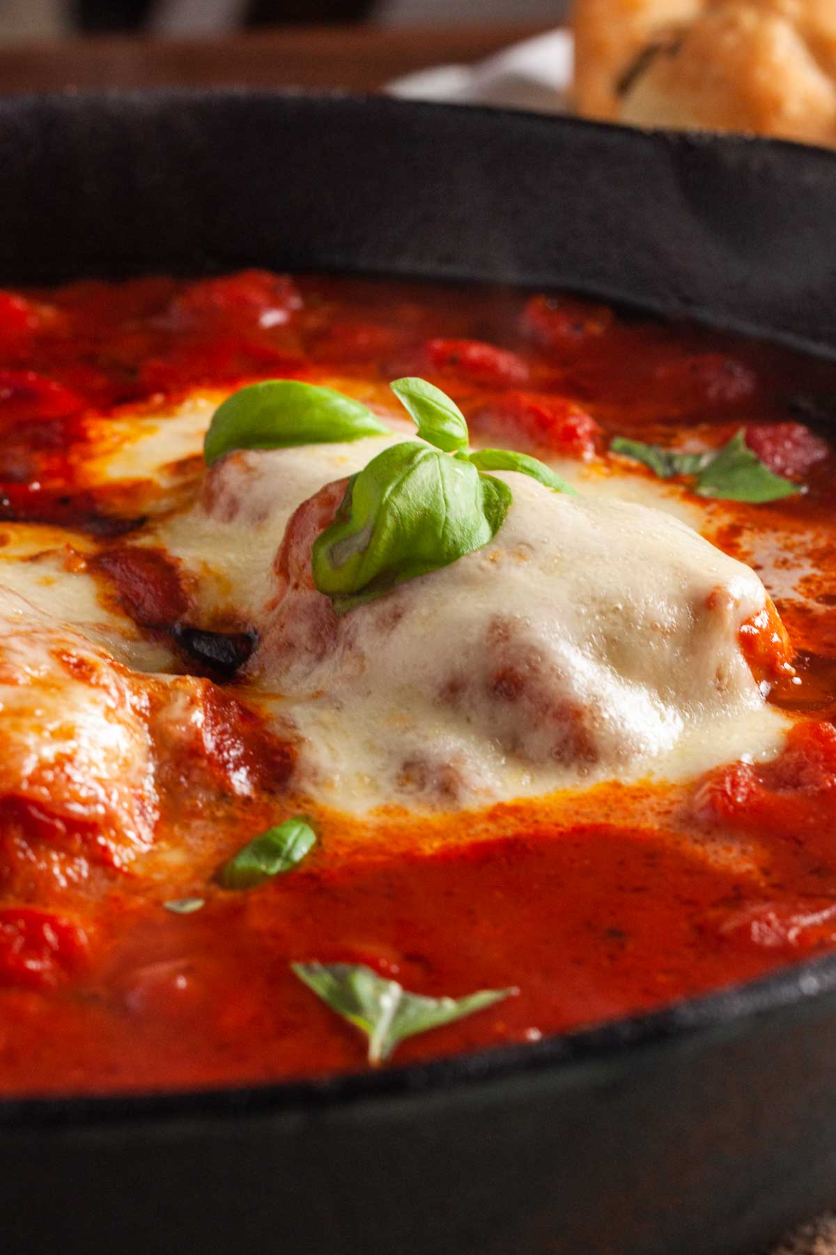 Closeup of chicken pizzaiola or chicken smothered in mozzarella and surrounded with tomato sauce in a cast iron pan.