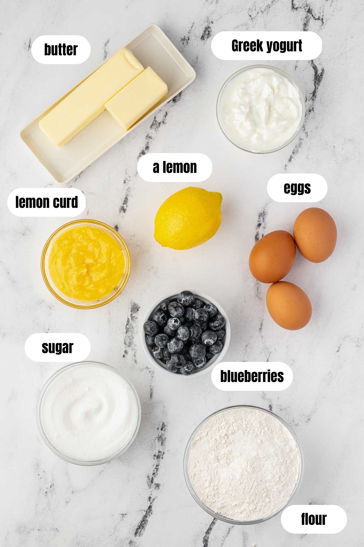Overhead collage of all the ingredients needed for a lemon curd cake with blueberries including flour, butter, sugar, lemon, blueberries, lemon curd, eggs and Greek yogurt.