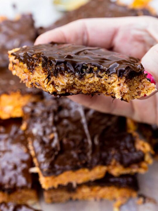 Closeup of someone holding a peanut butter cornflake bar with a bite out of it and with more bars below and around it.