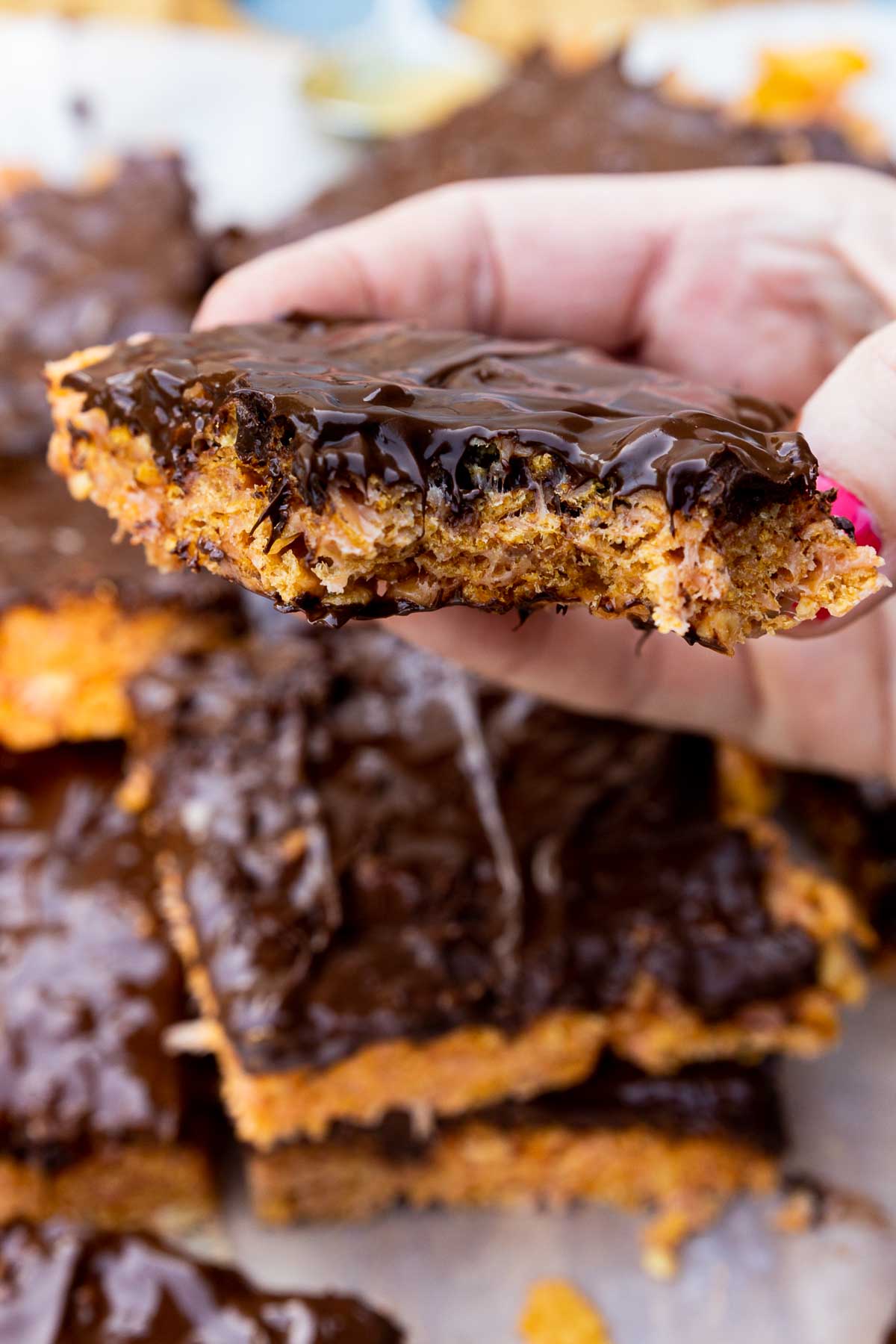 Closeup of someone holding a peanut butter cornflake bar with a bite out of it and with more bars below and around it.